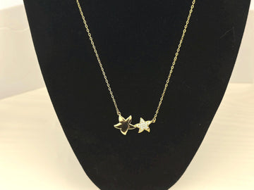 18K gold filled necklace with double star pendant. The stars are of different sizes sitting side by side. The larger star is a smooth gold surface, the second smaller star sparkling gemstones.The necklace hung on a black prop to emphasize the beauty of the necklace.