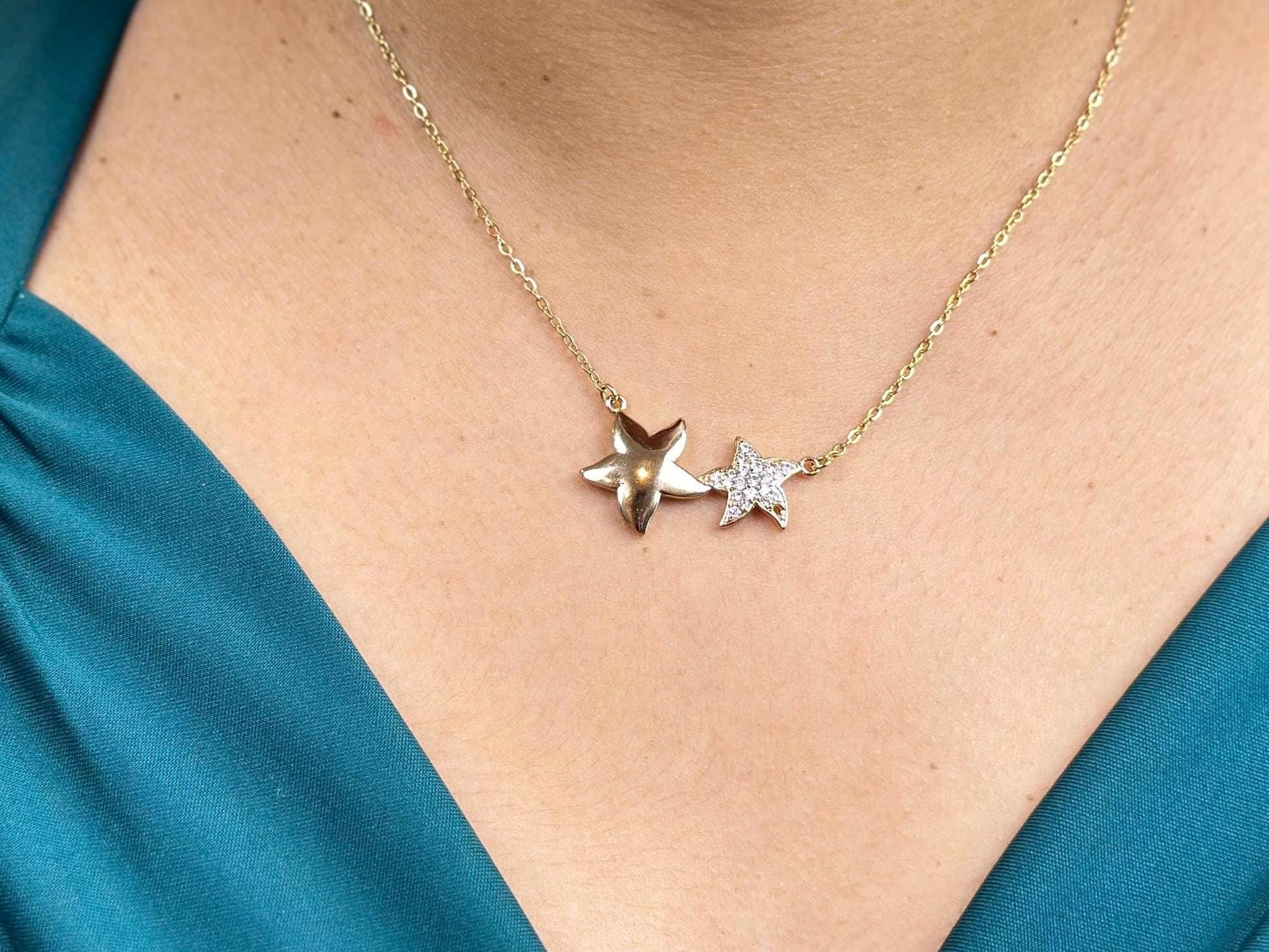 18K gold filled necklace with double star pendant on a model's neck. The stars are of different sizes sitting side by side. The larger star is a smooth gold surface, the second smaller star sparkling gemstones.