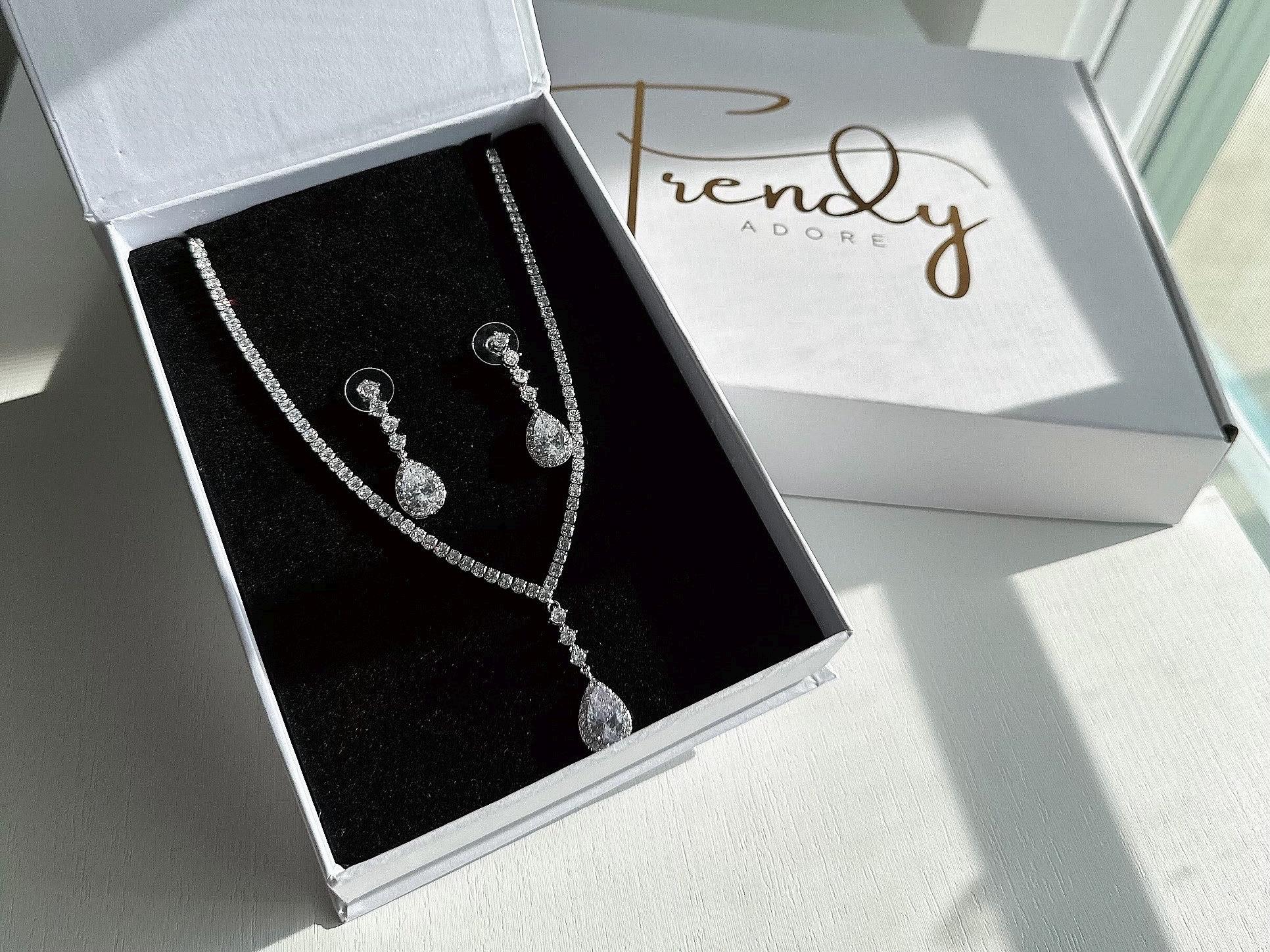 An elegant dainty sparkly diamond silver  earrings and a matching necklace with a pendant in a white jewelry box branded with TrendyAdore logo in Gold. The jewelry box is magnetic and has high quality black foam padding that protects the jewelry set