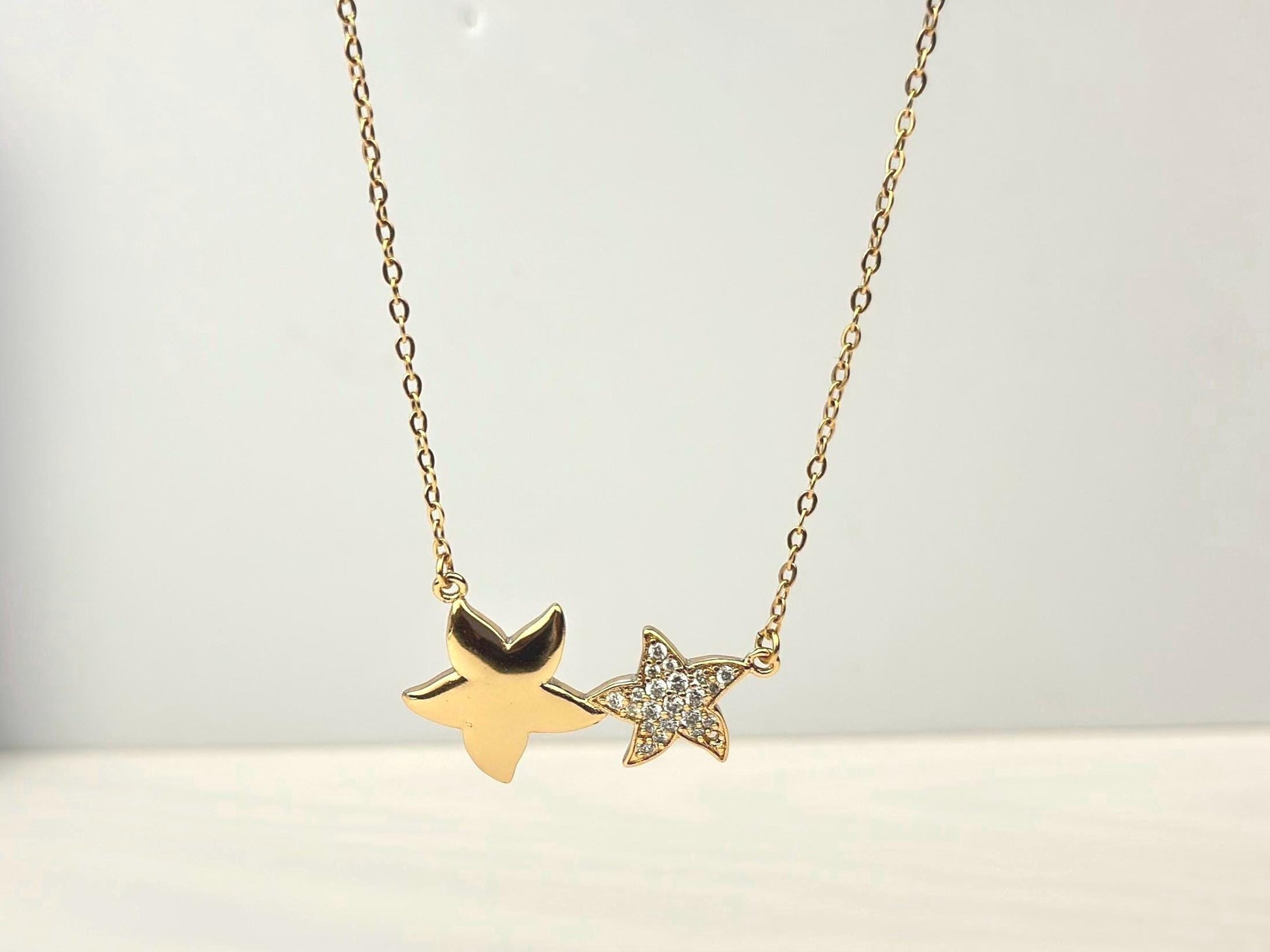 18K gold filled necklace with double star pendant. The stars are of different sizes sitting side by side. The necklace hanging freely in the air with a white background to emphasize the beauty of the necklace