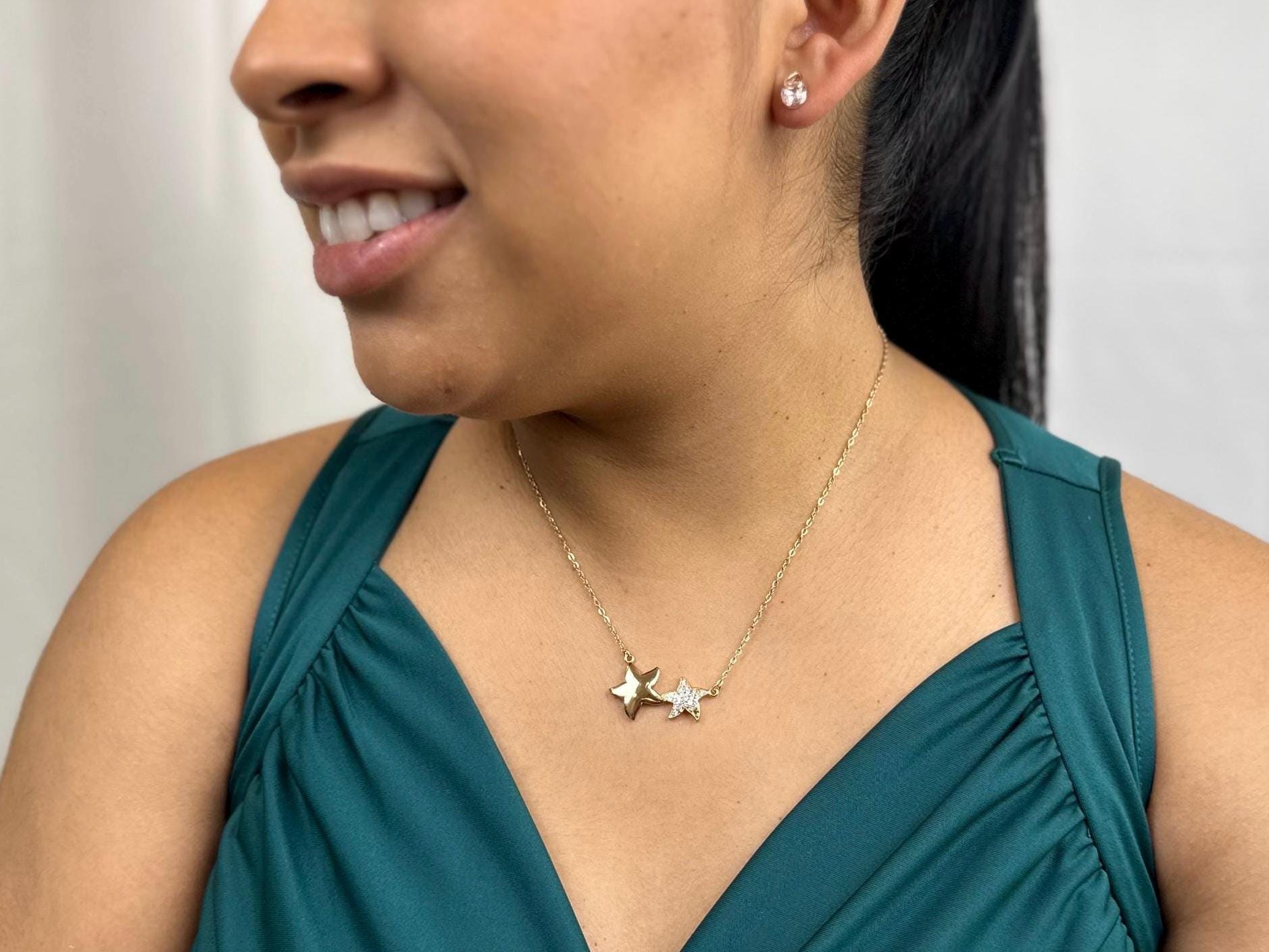 18K gold filled necklace with double star pendant on a model's neck. The stars are of different sizes sitting side by side. This image shows half of the model's face with a beautiful smile