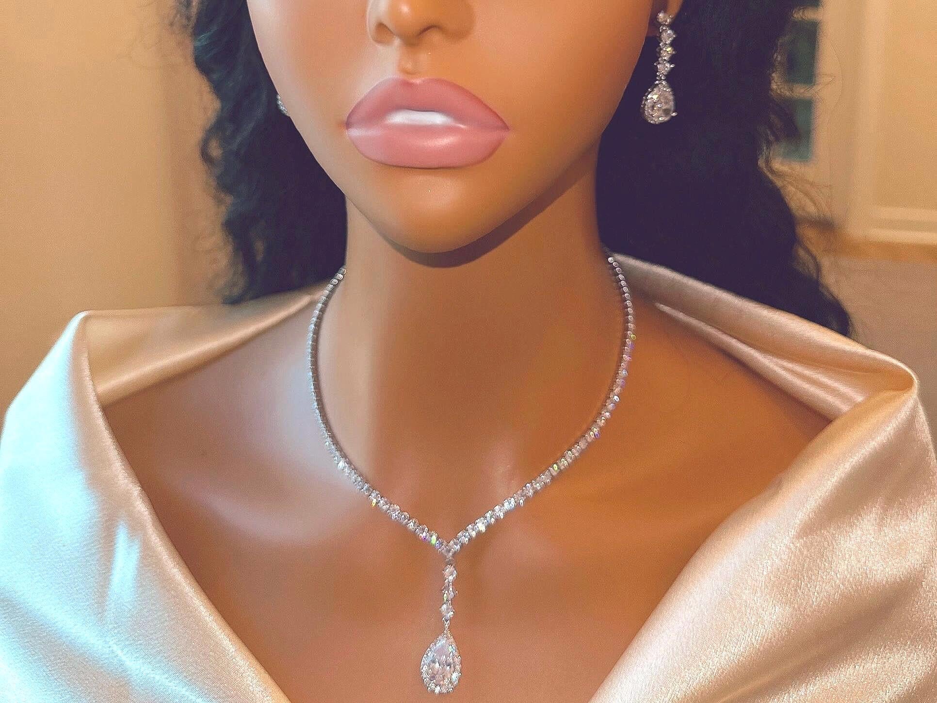 Close-up of a face and neck showcasing elegant dainty diamond sparkly teardrop earrings and a matching necklace with a pendant.