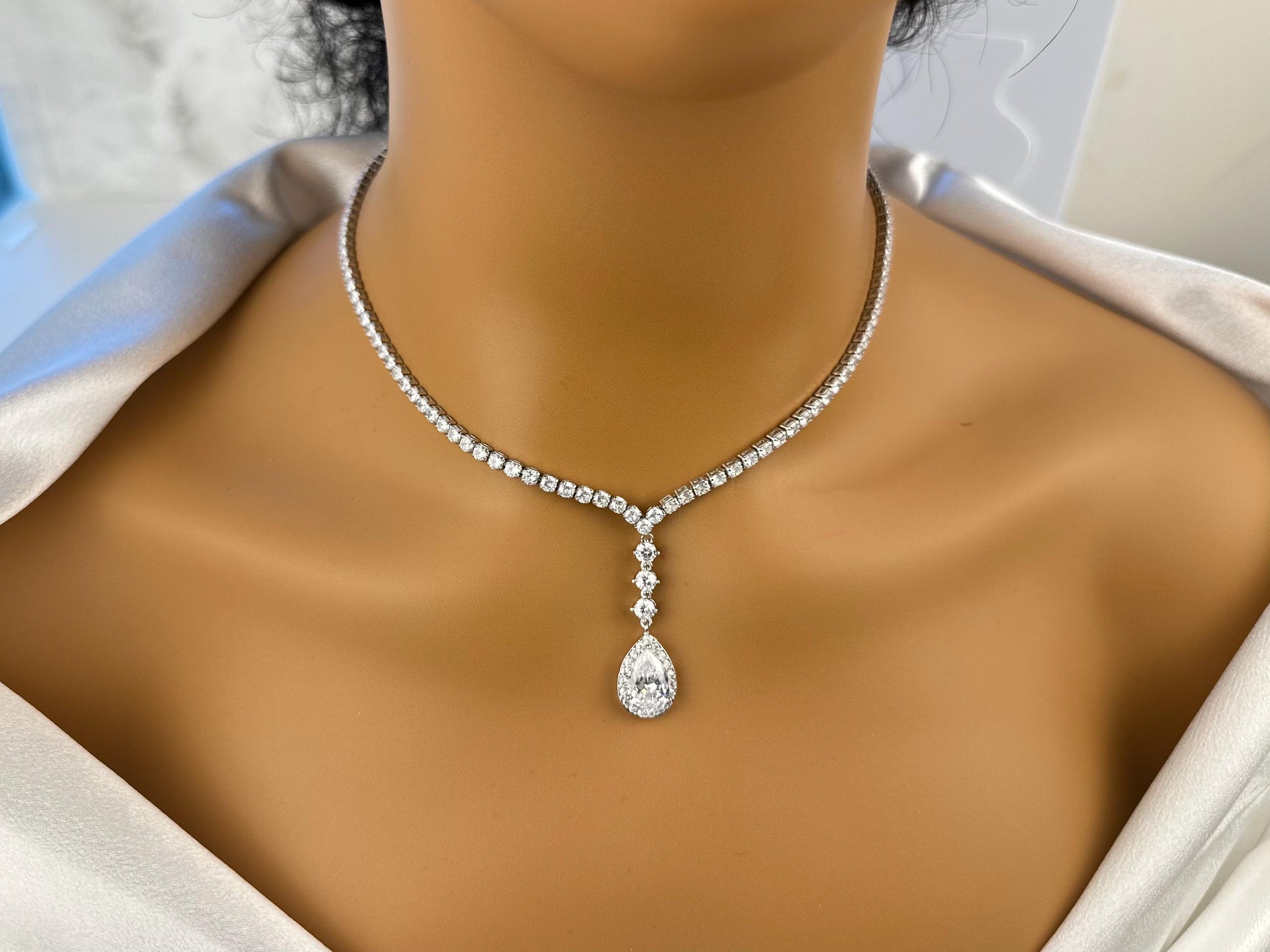 Close-up of elegant dainty diamond sparkly teardrop silver pendant and necklace on a neckline.