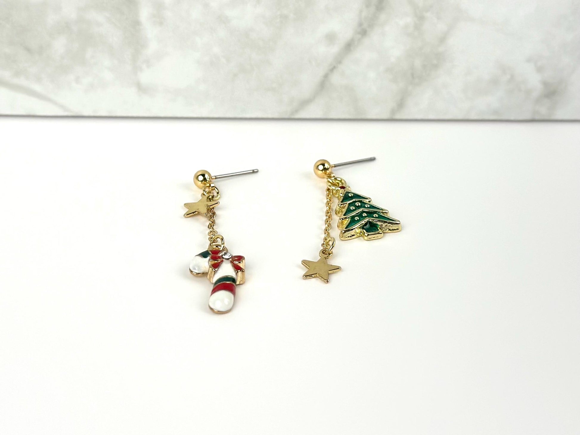 mismatched dangle earrings on a white surface, about 2 inches long, one earring with white green and red candy cane and gold star charm and the other earring with green Christmas tree and gold star charm