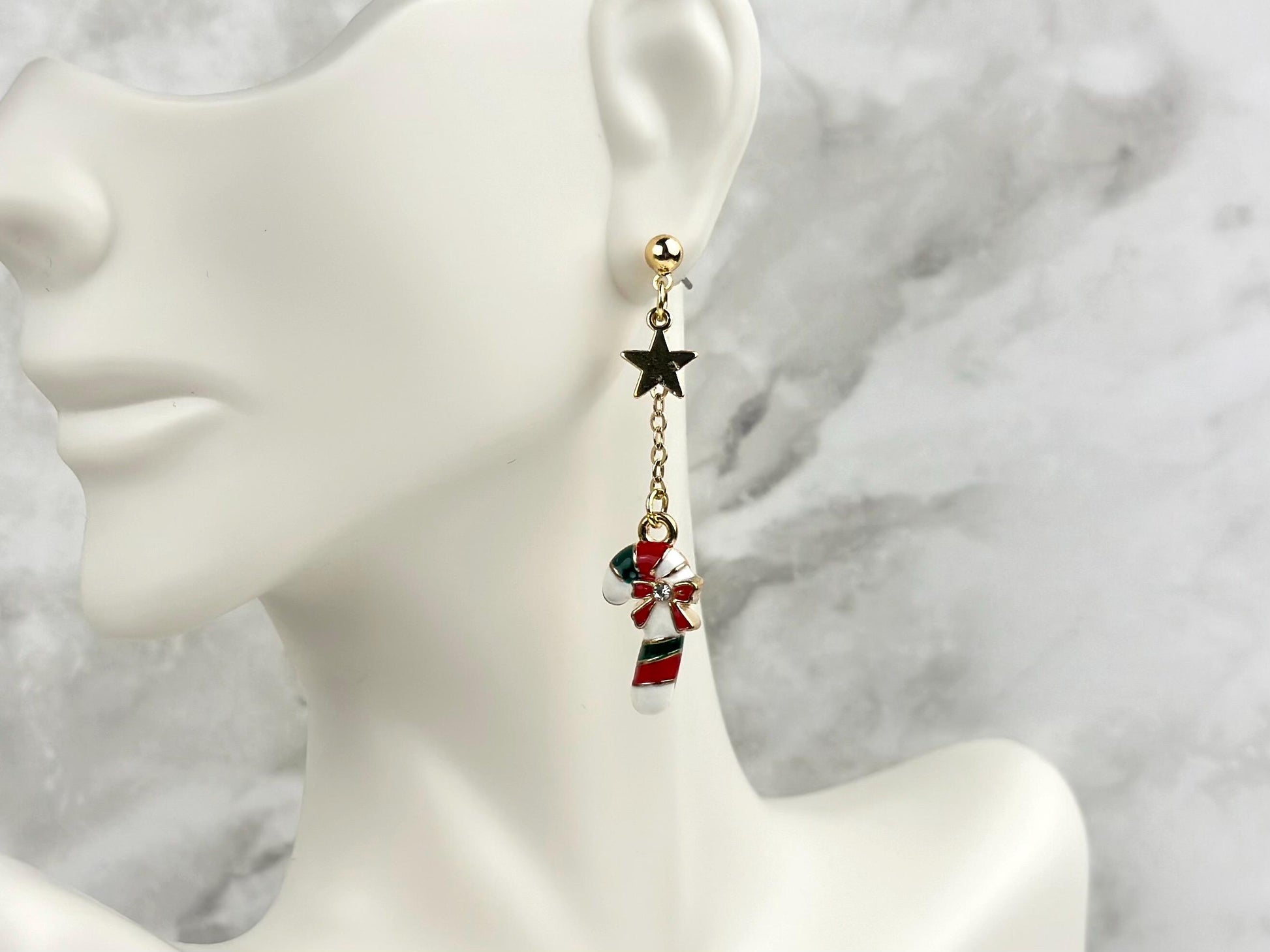 Red, green and white candy cane and gold star charm earrings worn on a white Mannikin’s earlobe. It has a beautiful Christmas earring feel.