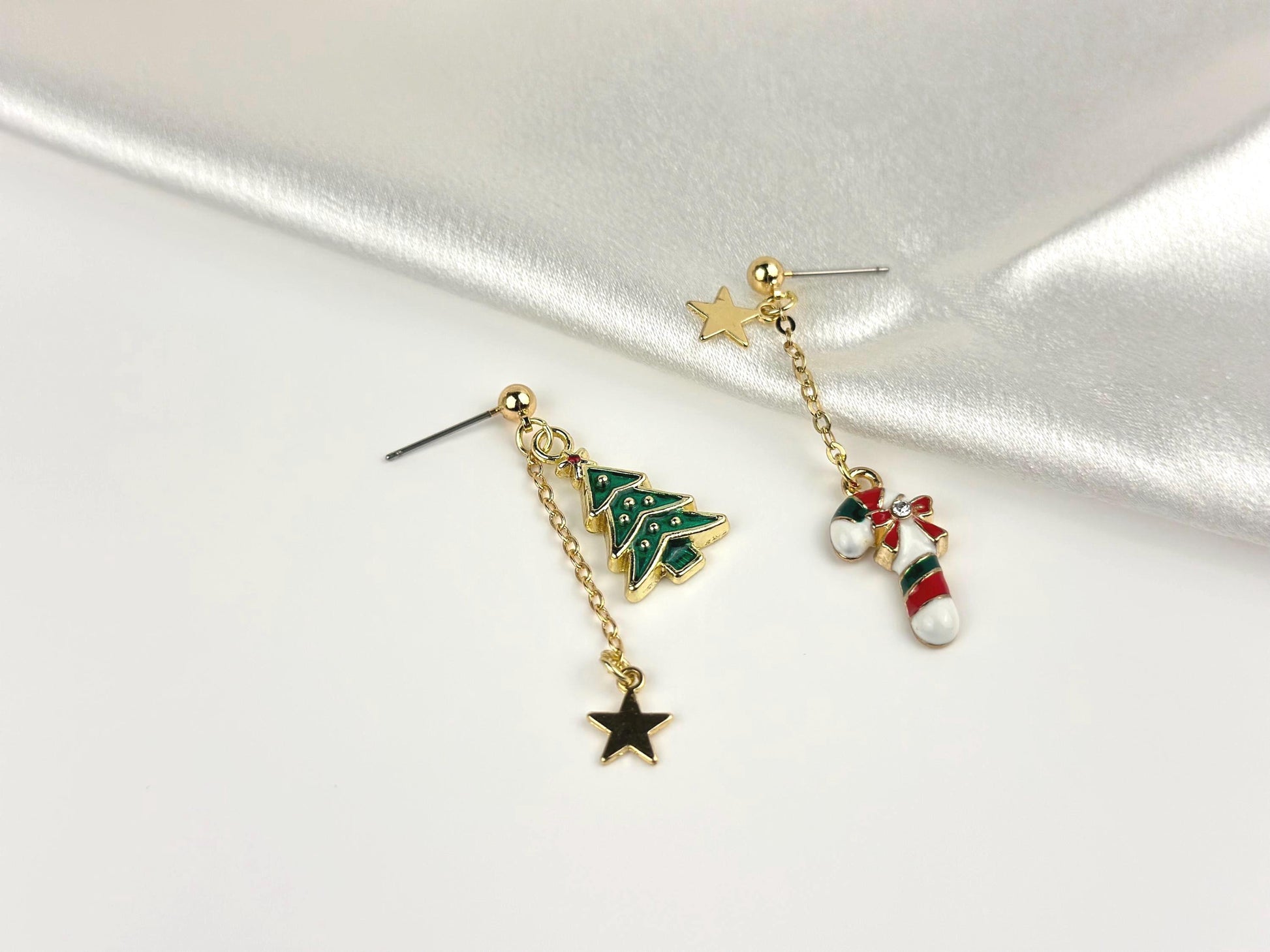 mismatched dangle earrings on a satin fabric, about 2 inches long, one earring with white green and red candy cane and gold star charm and the other earring with green Christmas tree and gold star charm